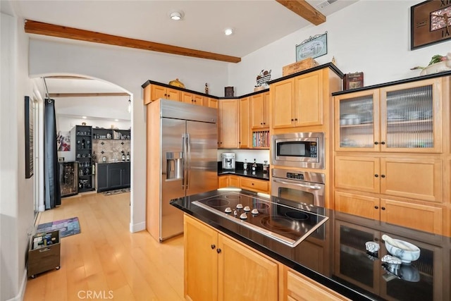 kitchen with light wood finished floors, arched walkways, dark countertops, beamed ceiling, and built in appliances