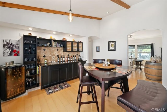 dining room with light wood finished floors, beam ceiling, arched walkways, and indoor wet bar