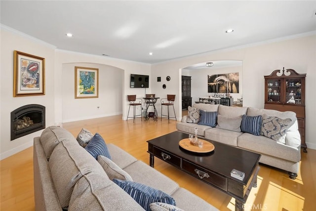 living room featuring arched walkways, a fireplace, light wood finished floors, recessed lighting, and ornamental molding