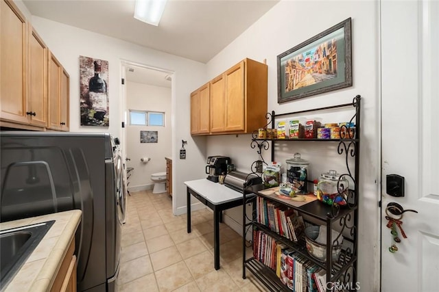 laundry area with light tile patterned floors, cabinet space, washing machine and dryer, a sink, and baseboards