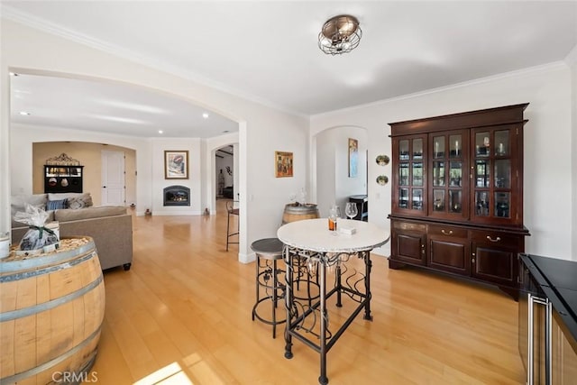 dining room featuring arched walkways, light wood-style flooring, baseboards, a lit fireplace, and ornamental molding