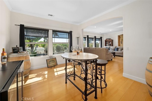 dining area with light wood finished floors, baseboards, visible vents, arched walkways, and crown molding