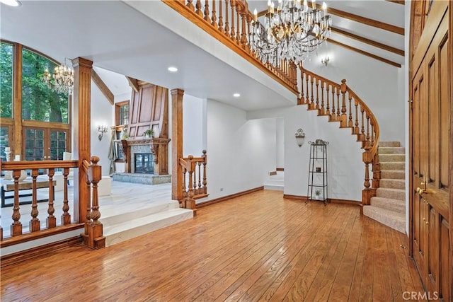 interior space with beam ceiling, a large fireplace, high vaulted ceiling, a chandelier, and wood-type flooring