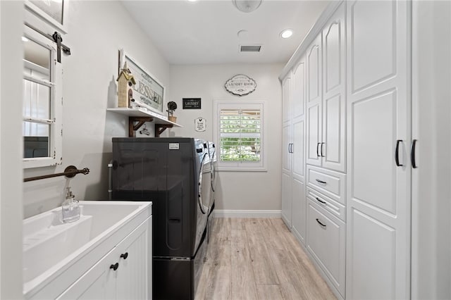 washroom featuring cabinets, washer and dryer, sink, a barn door, and light hardwood / wood-style flooring