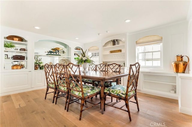 dining room with light wood-type flooring, built in features, and ornamental molding