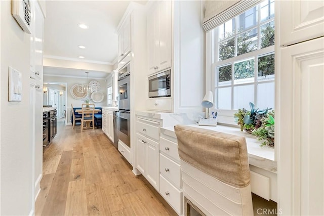 kitchen featuring appliances with stainless steel finishes, pendant lighting, an inviting chandelier, light hardwood / wood-style flooring, and white cabinetry