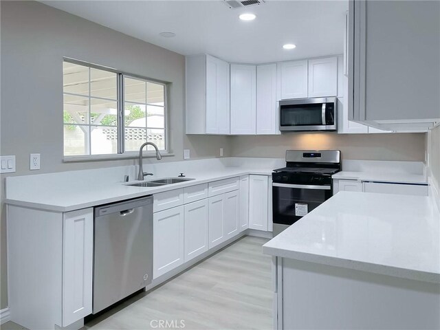 kitchen with light hardwood / wood-style floors, sink, white cabinets, and stainless steel appliances