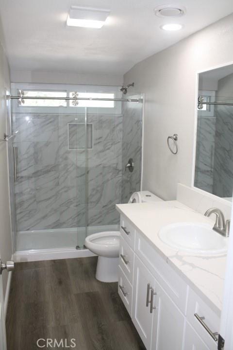 bathroom featuring hardwood / wood-style flooring, vanity, a shower with shower door, and toilet