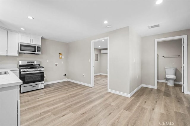 kitchen with light stone countertops, appliances with stainless steel finishes, white cabinets, and light wood-type flooring