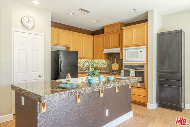 kitchen featuring a kitchen island with sink, stainless steel appliances, tasteful backsplash, light tile patterned flooring, and a kitchen bar