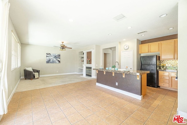 kitchen with ceiling fan, black fridge, a kitchen island with sink, and light brown cabinets