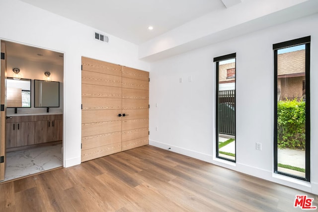 unfurnished bedroom featuring multiple windows, hardwood / wood-style flooring, and ensuite bathroom