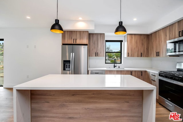 kitchen featuring sink, light hardwood / wood-style flooring, appliances with stainless steel finishes, a kitchen island, and decorative light fixtures