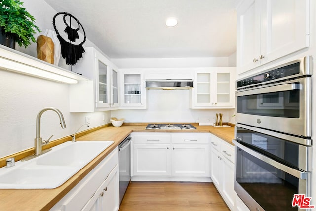 kitchen featuring appliances with stainless steel finishes, ventilation hood, white cabinetry, sink, and light hardwood / wood-style floors