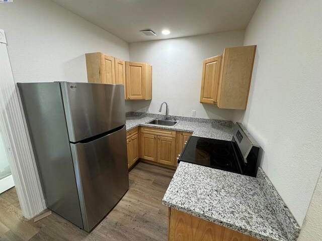 kitchen featuring light stone countertops, sink, light hardwood / wood-style flooring, black electric range oven, and stainless steel fridge