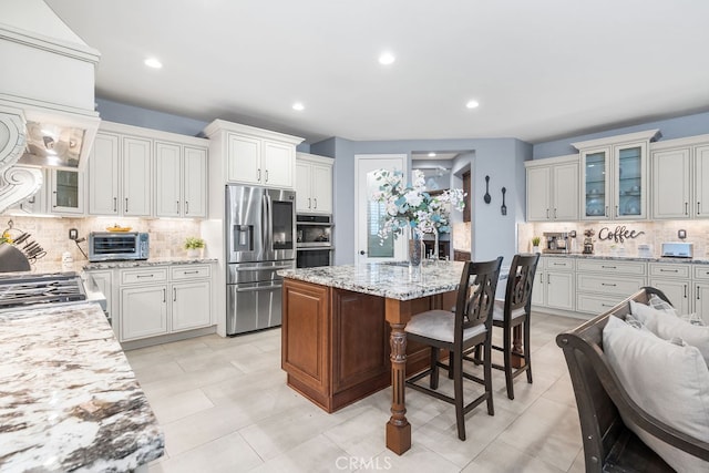 kitchen featuring a breakfast bar area, an island with sink, light stone countertops, white cabinetry, and appliances with stainless steel finishes