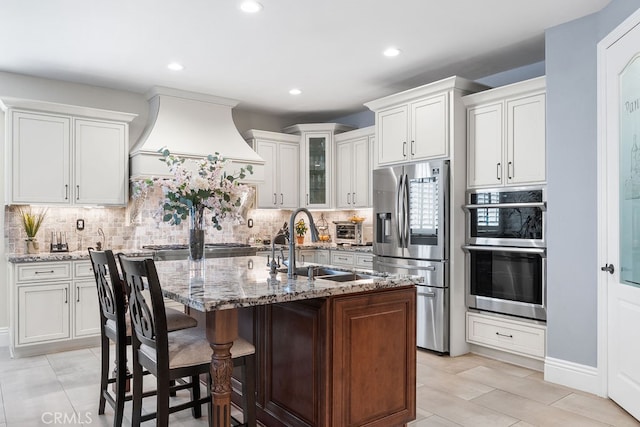 kitchen with white cabinets, a center island with sink, light stone counters, a kitchen breakfast bar, and stainless steel appliances