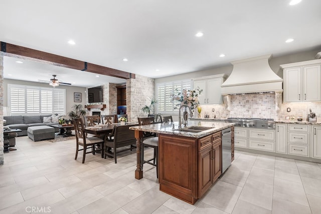 kitchen with premium range hood, a healthy amount of sunlight, sink, and a center island with sink