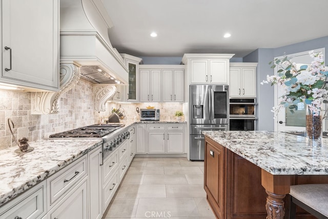 kitchen featuring white cabinets, tasteful backsplash, premium range hood, light stone countertops, and stainless steel appliances