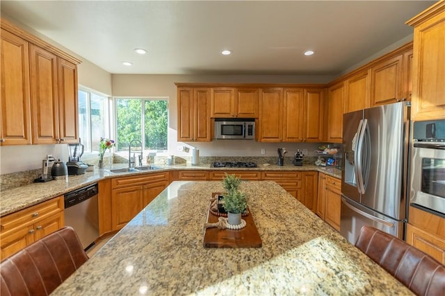 kitchen featuring a kitchen bar, stainless steel appliances, light stone counters, and sink