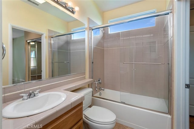 full bathroom with bath / shower combo with glass door, vanity, and toilet