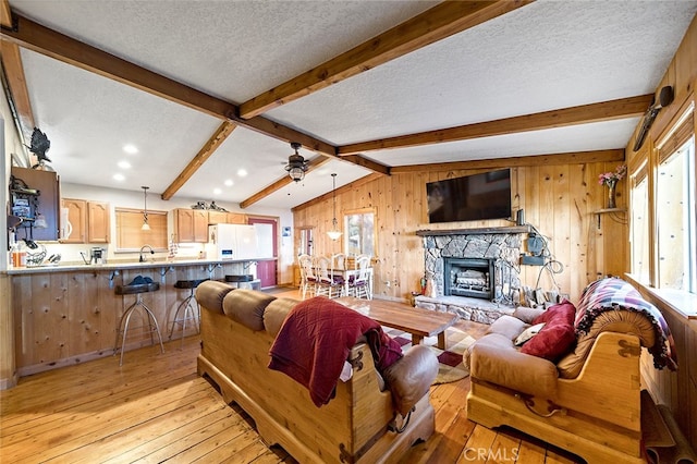 living room with ceiling fan, vaulted ceiling with beams, light wood-type flooring, a textured ceiling, and a fireplace