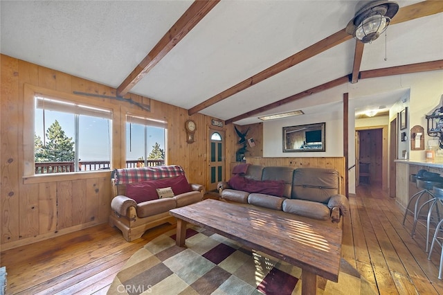 living room featuring lofted ceiling with beams, light hardwood / wood-style floors, a textured ceiling, wooden walls, and ceiling fan