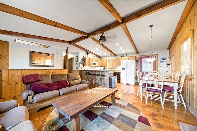 living room with ceiling fan, vaulted ceiling with beams, wooden walls, and light hardwood / wood-style flooring