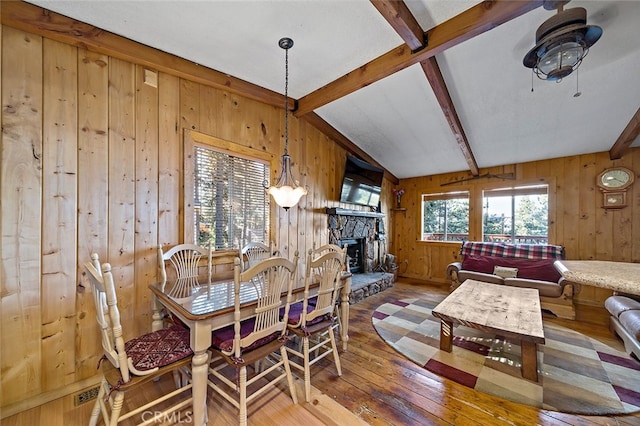 dining area featuring lofted ceiling with beams, wood-type flooring, wood walls, a fireplace, and ceiling fan