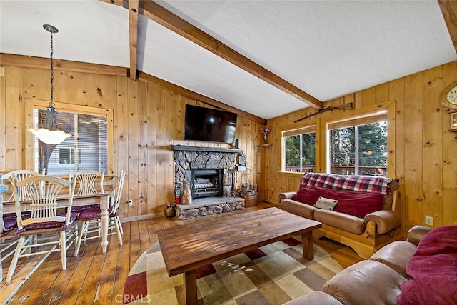 living room with lofted ceiling with beams, wooden walls, hardwood / wood-style flooring, and a stone fireplace