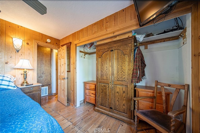 bedroom with a textured ceiling, wooden walls, light hardwood / wood-style flooring, and a closet