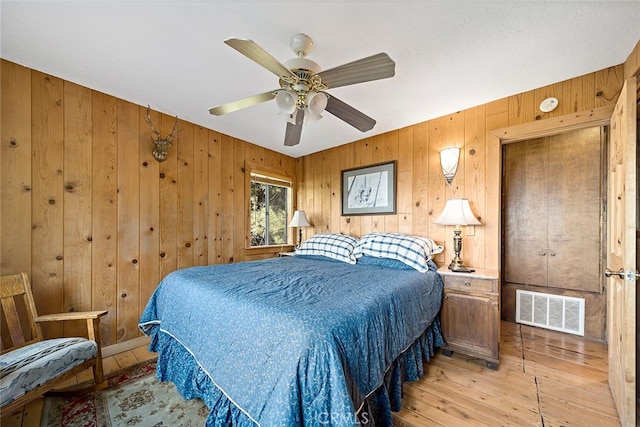 bedroom featuring ceiling fan, wood walls, and light hardwood / wood-style floors