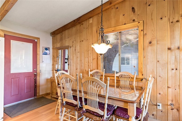 dining room with wooden walls, beamed ceiling, and hardwood / wood-style floors