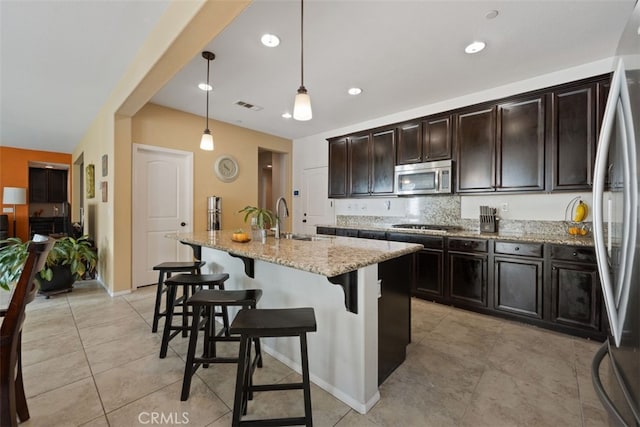 kitchen featuring sink, hanging light fixtures, a kitchen bar, a kitchen island with sink, and appliances with stainless steel finishes