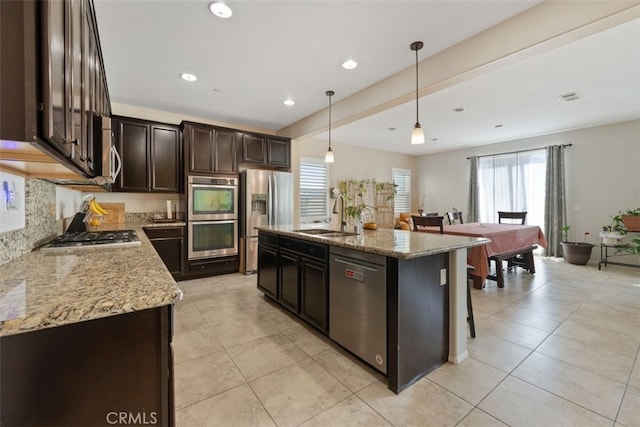 kitchen with pendant lighting, a kitchen island with sink, sink, light stone countertops, and stainless steel appliances