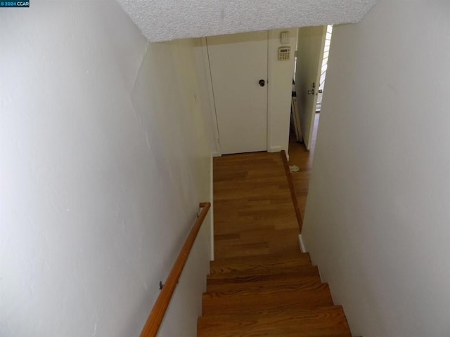 stairway with a textured ceiling and hardwood / wood-style flooring