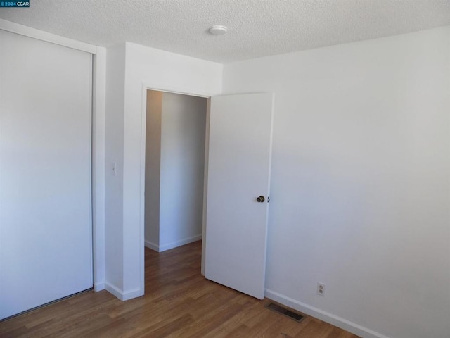 unfurnished bedroom with hardwood / wood-style floors, a textured ceiling, and a closet