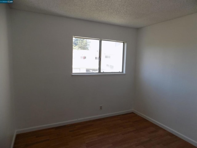 spare room with a textured ceiling and dark hardwood / wood-style floors