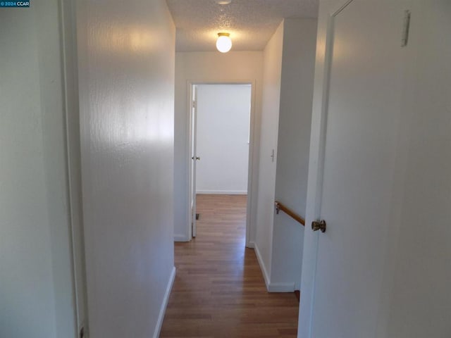 hall with wood-type flooring and a textured ceiling