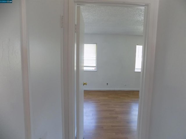 corridor with a textured ceiling and light wood-type flooring