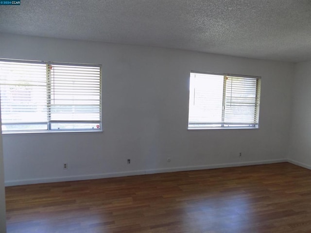 empty room with a textured ceiling, dark hardwood / wood-style flooring, and a wealth of natural light