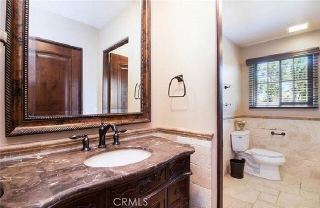 bathroom featuring toilet, vanity, and tile walls