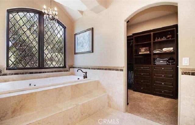 bathroom with a relaxing tiled tub, an inviting chandelier, and tile walls