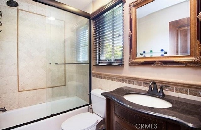 full bathroom with vanity, combined bath / shower with glass door, toilet, and tile walls