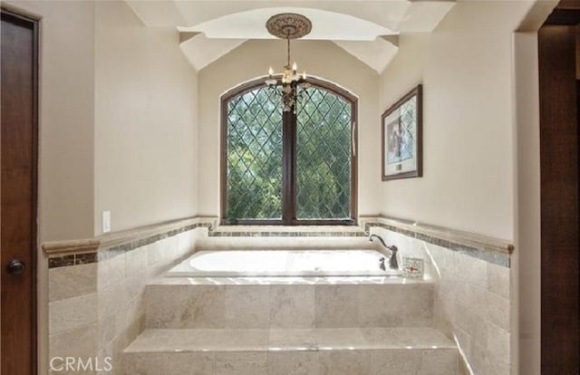 bathroom featuring a chandelier, tiled bath, and vaulted ceiling