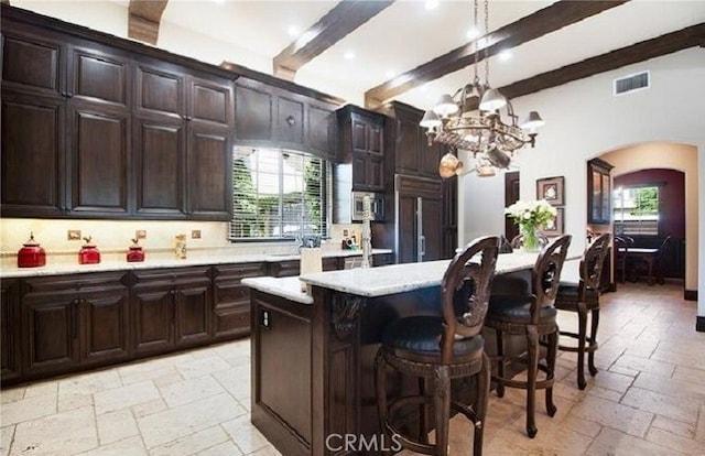 kitchen with a breakfast bar area, decorative light fixtures, paneled built in fridge, a kitchen island, and beam ceiling