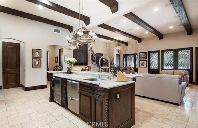 kitchen with sink, hanging light fixtures, a kitchen island with sink, light stone counters, and dark brown cabinets