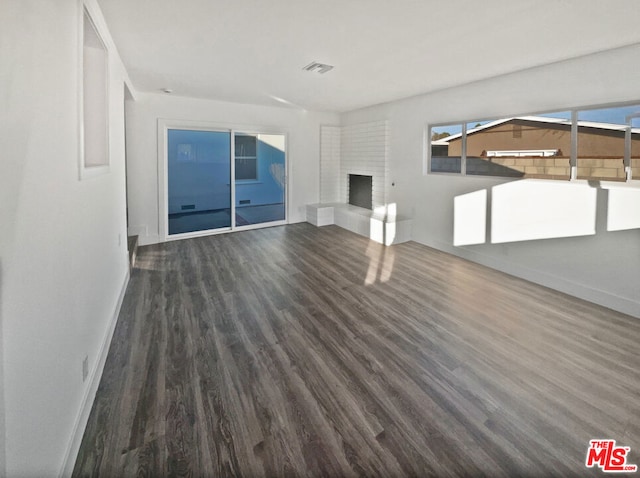 unfurnished living room with dark hardwood / wood-style flooring and a brick fireplace