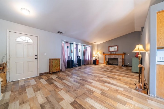 foyer with light wood-type flooring, lofted ceiling, and a tile fireplace