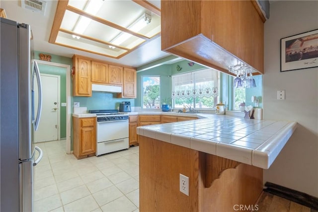 kitchen with sink, tile counters, white range oven, kitchen peninsula, and stainless steel refrigerator